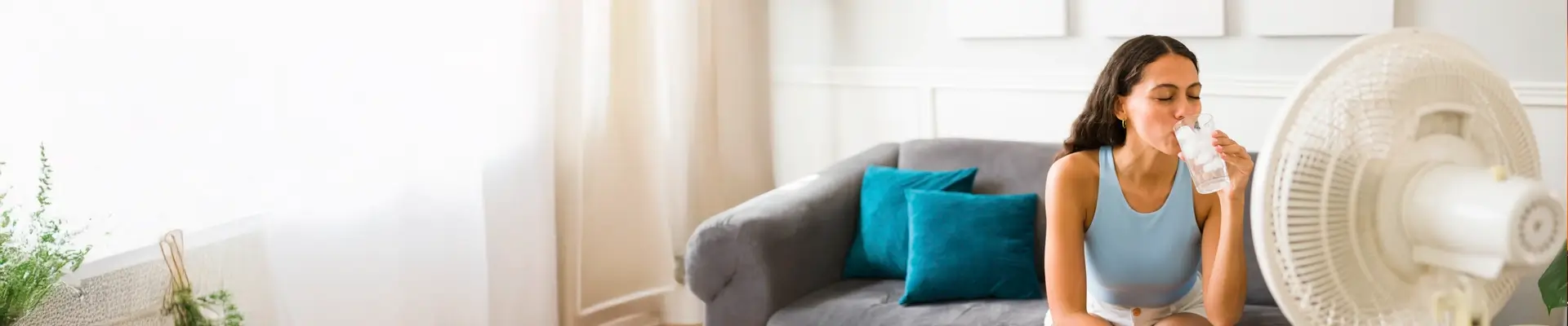 BlueChip Energy & Climate Solutions - Contact page image of a sitting in her living room drinking icy cold water in a glass in front of a fan to keep cool.